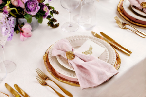 Gold-rimmed place setting with pink linen napkin and floral centrepiece